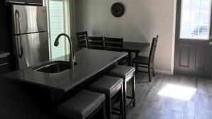 A modern kitchen with a stainless steel refrigerator, a sink, and a dining area with a table and chairs.