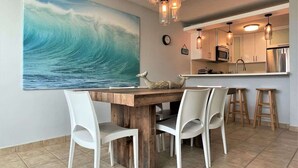 A dining area with a wooden table and white chairs, a kitchen with modern appliances, and a large wave painting on the wall. - #1 Luxury 4BR Rooftop Penthouse @ Jobos Beach (Isabela)