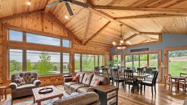 A spacious living room with wooden floors, large windows, and a dining area with wooden furniture.