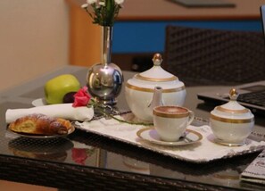 A breakfast setup with a croissant, a cup of coffee, a teapot, and a vase with flowers on a table. - Hotel Resort Il Panfilo (Giugliano in Campania)