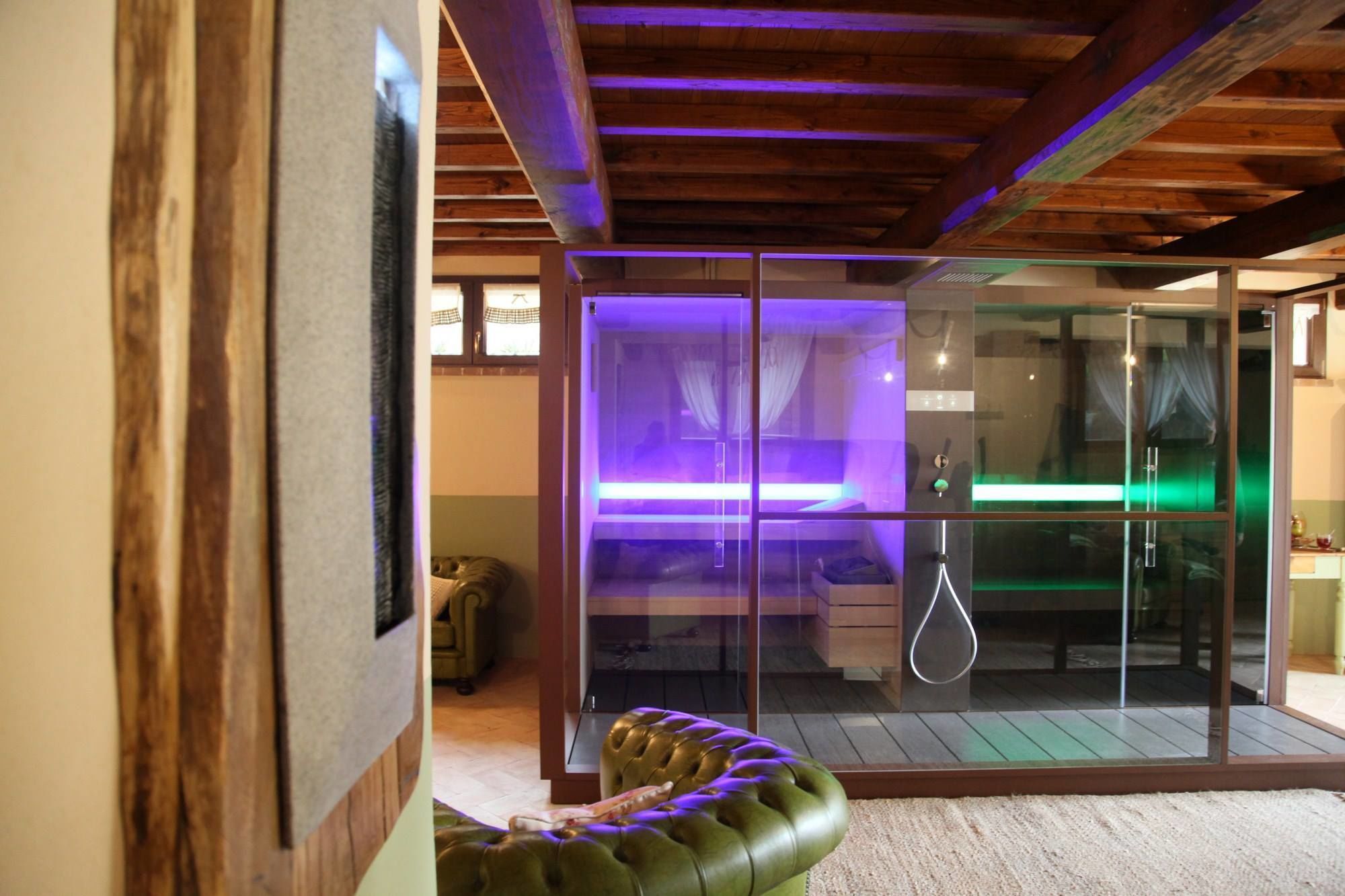 A modern bathroom with a glass shower enclosure, wooden beams, and a green leather bench.