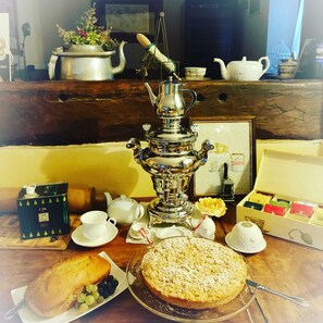 A table set with a samovar, teapot, cups, saucers, a box of tea, a cake, and a plate of fruit.