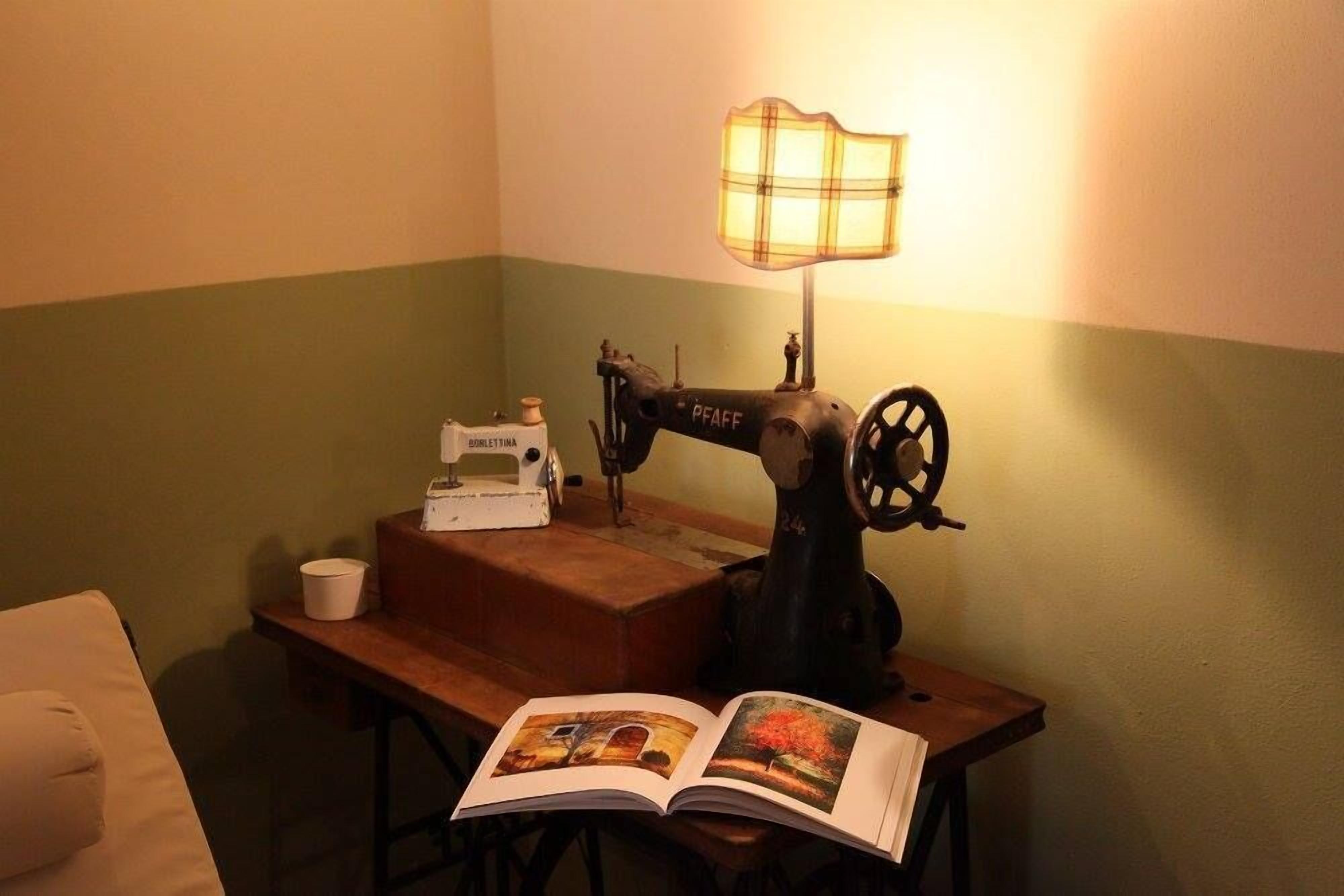 A sewing machine on a wooden table with a lamp, a book, and a cup.