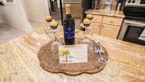 Een keukenblad met een fles Oak Leaf Vineyard Merlot, een welkomstkaart en drie cupcakes op een decoratieve mat.