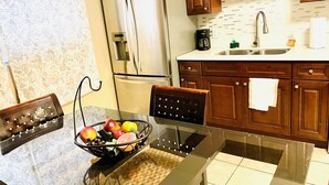 A modern kitchen with wooden cabinets, a stainless steel refrigerator, a glass dining table with a fruit bowl, and a coffee maker. - STRIP 2BR Condo NEARLVCC pet-Friendly Free-wifi on SALE Vegas music festival (Las Vegas)
