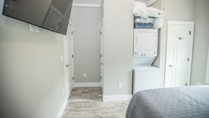 A bedroom with a bed, a washing machine, and a television mounted on the wall. - Coop's Coop: A newly renovated studio cottage (Hendersonville)