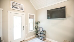A hallway with a door, a window with a plant, a welcome sign, and a mounted TV. - Coop's Coop: A newly renovated studio cottage (Hendersonville)