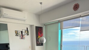Una sala de estar moderna con una mesa de comedor de vidrio, un sofá marrón oscuro y vista al océano a través de una puerta corrediza de vidrio.