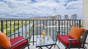 A balcony with two red cushioned chairs, a glass table, and a bottle of water. - Great for Families! Partial Ocean/Canal/Diamond Head Views! Pool/WiFi/Parking (Honolulu)