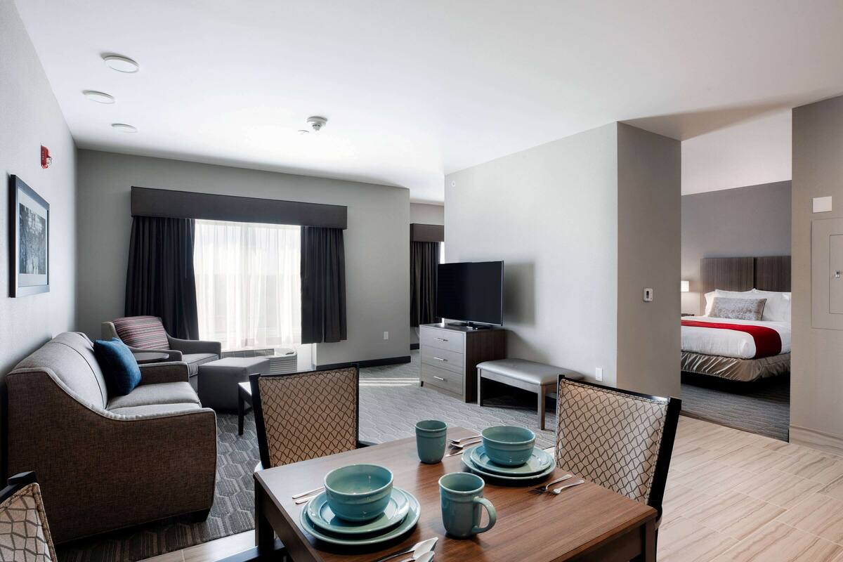 A modern hotel room with a dining area, a sofa, a TV, and a bed with a red accent.