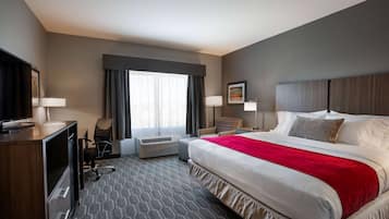 Una habitación de hotel con una cama grande, un escritorio con televisor, una silla, una ventana con cortinas y un equipo de aire acondicionado.