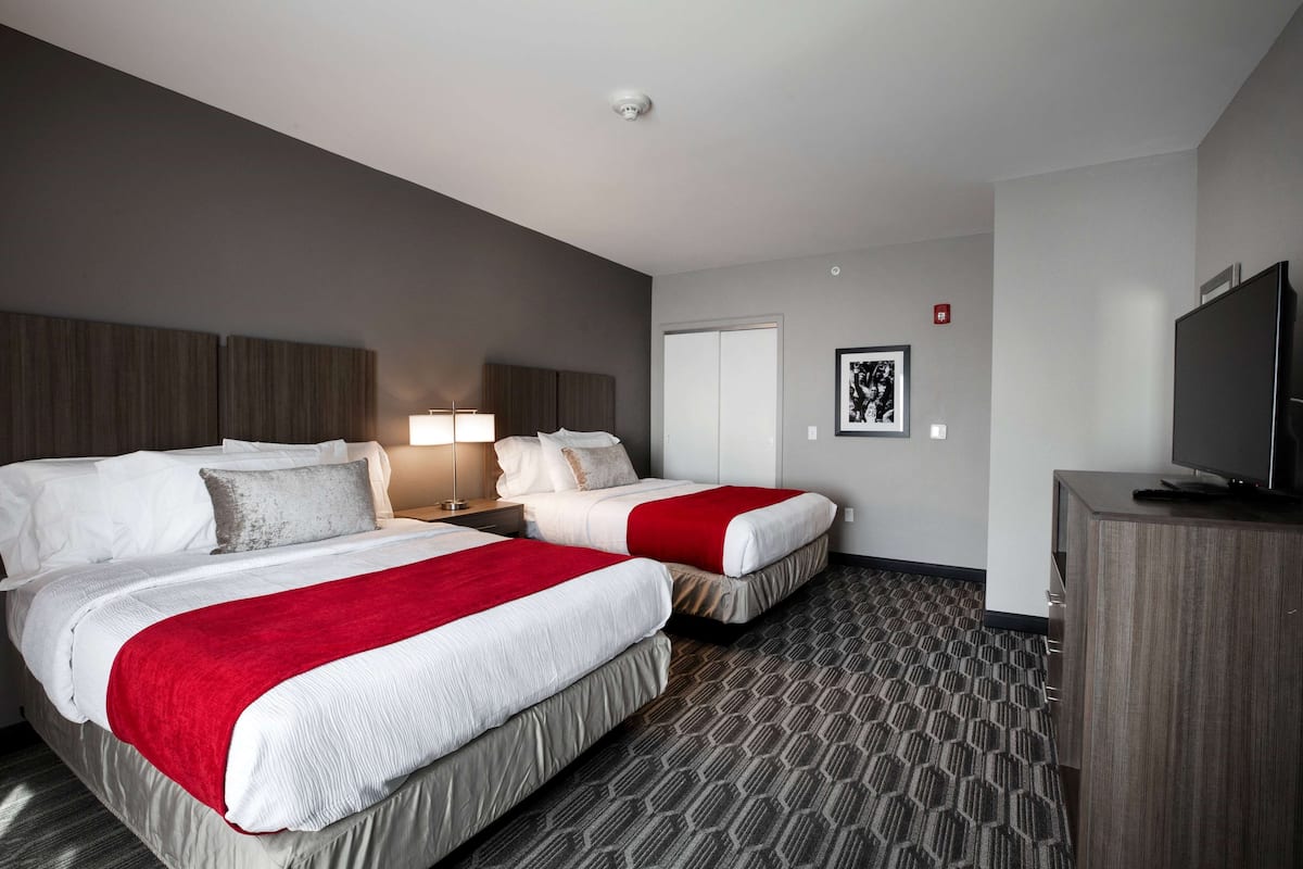 A hotel room with two beds, a TV, a desk, and a lamp.