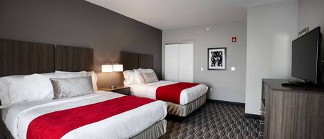 A hotel room with two beds, a TV, a desk, and a lamp.