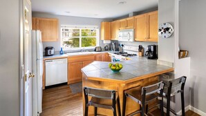 A modern kitchen with wooden cabinets, a central island with bar stools, a microwave, and a world map clock. - Super Location, Free Parking, 3 Bedroom + Loft, 3.5 Ba, Sleeps 10, Tesla Charger (Seattle)