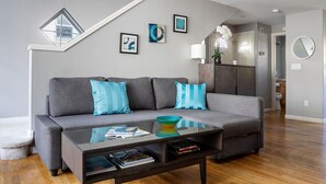 A modern living room with a grey sofa, blue cushions, a glass coffee table, and wooden flooring. - Super Location, Free Parking, 3 Bedroom + Loft, 3.5 Ba, Sleeps 10, Tesla Charger (Seattle)