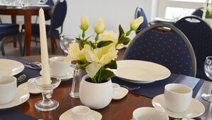 A dining table set with white plates, bowls, and cups, a candle, and a vase with yellow flowers. - Hotel B8 Voerde (Voerde)