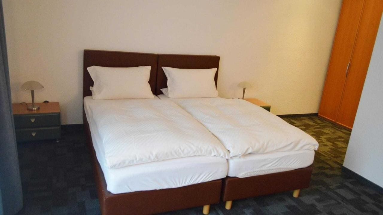 A double bed with white bedding, a wooden headboard, and a nightstand with a lamp.