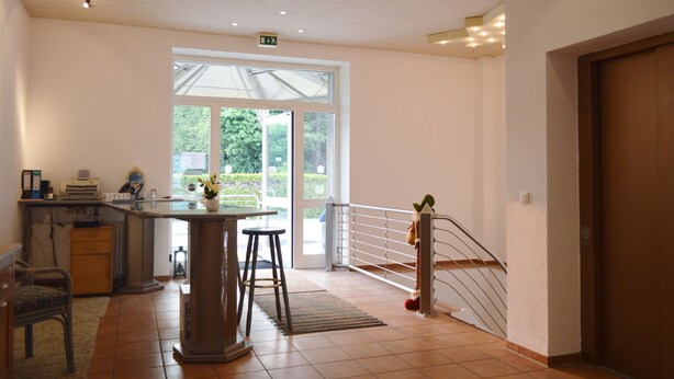 A spacious room with a large window, a desk with a chair, a small table with stools, and a staircase with a railing. - Hotel B8 Voerde (Voerde)