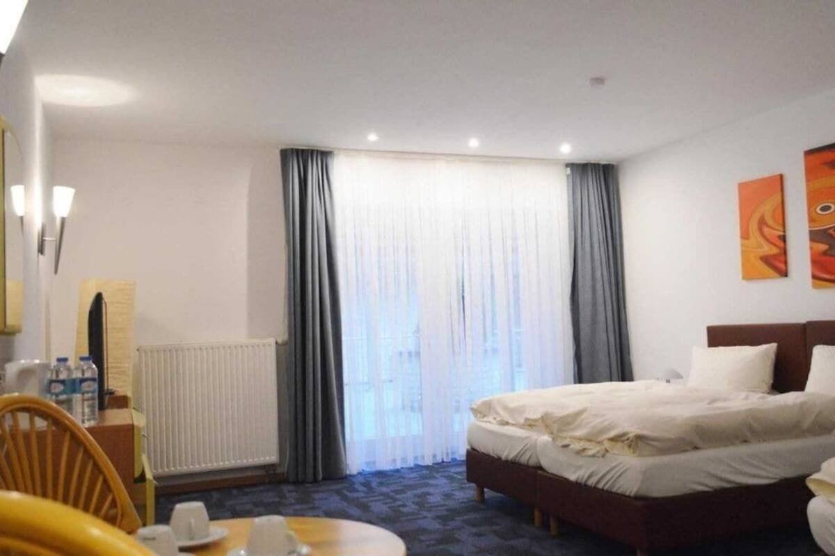 Una habitación de hotel con cama, una silla, una mesa con tazas, un radiador y cortinas.