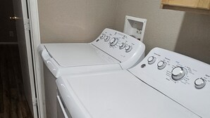 A front view of a white front-loading washer and dryer unit with control knobs and a power outlet. - Ranch House (Thompson Springs)