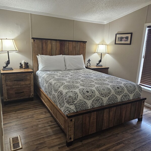 A bedroom with a wooden bed frame, two bedside tables with lamps, a wooden nightstand, and a window with blinds. - Ranch House (Thompson Springs)
