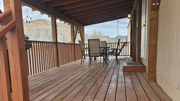 A wooden deck with a table and chairs, overlooking a mountainous landscape. - Ranch House (Thompson Springs)