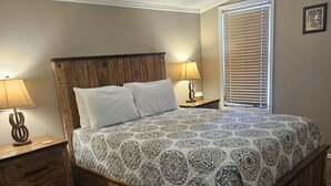 A bedroom with a wooden bed frame, two bedside tables with lamps, a window with blinds, and a patterned bedspread. - Ranch House (Thompson Springs)