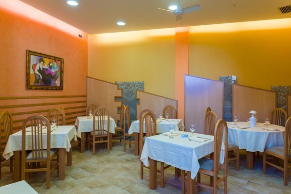 A restaurant interior with multiple tables and chairs, a ceiling fan, and a painting on the wall.