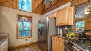 A kitchen with wooden cabinets, a stainless steel refrigerator, an oven, and a window with a view of trees. - PRIVATE LOG CABIN l PET FRIENDLY | HOT TUB l SAUNA (Cleveland)