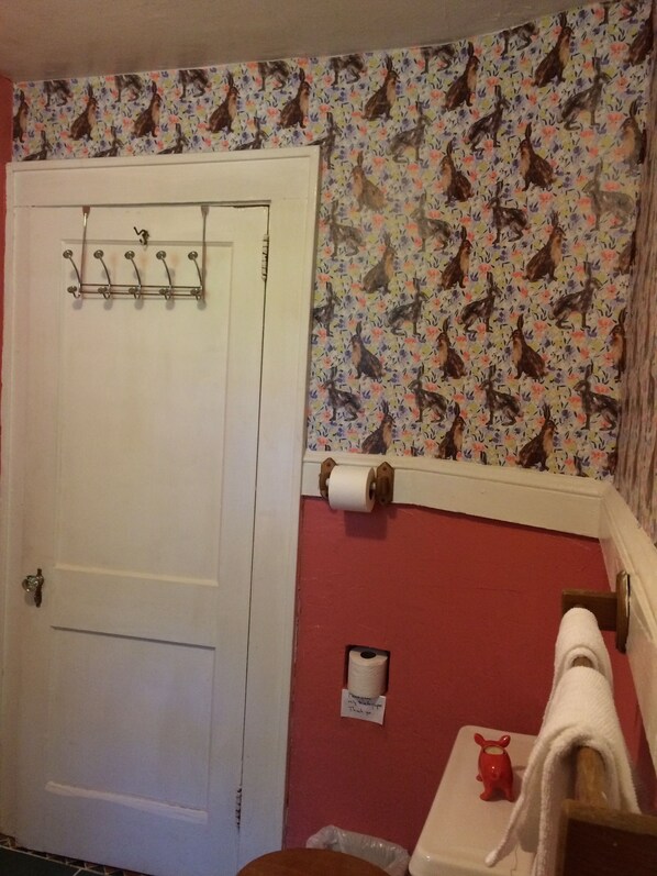 Une salle de bain avec une porte blanche, un porte-serviettes, un support à papier toilette et un mur rouge orné d’un motif floral.