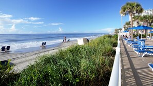Un hotel frente a la playa con un paseo mar ítimo, sillas y sombrillas.