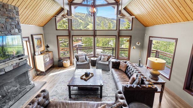 A spacious living room with a fireplace, large windows, and a high ceiling.