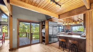 A modern kitchen with a large island, wooden ceiling, and a view of the outdoors.