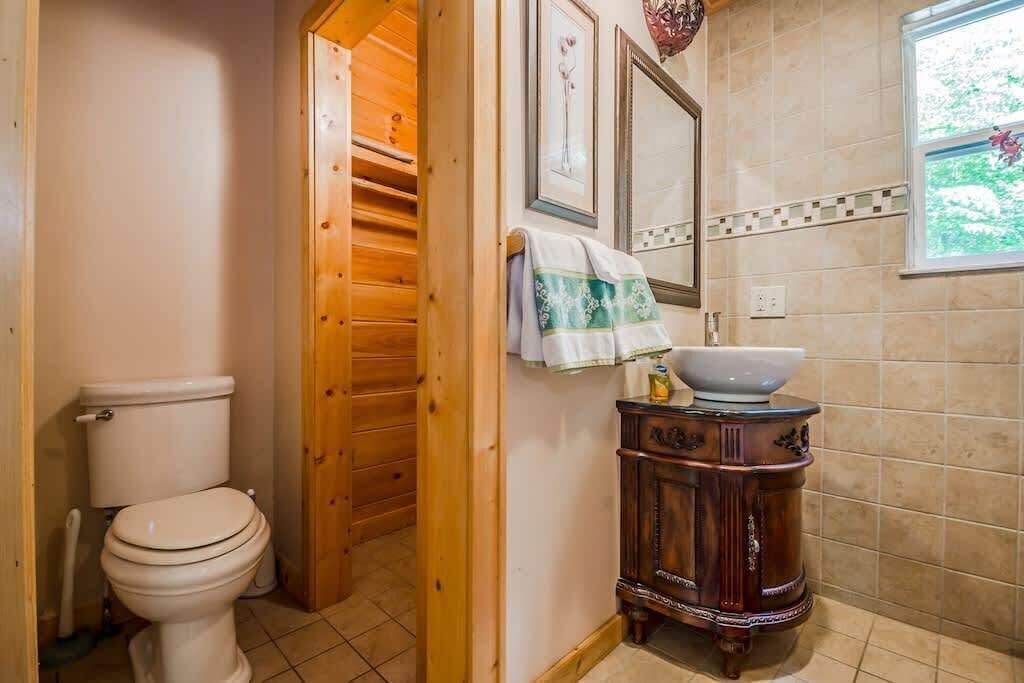 Et badeværelse med toilet, en trædør, vaskemøbel med håndvask og et vindue med udsigt.