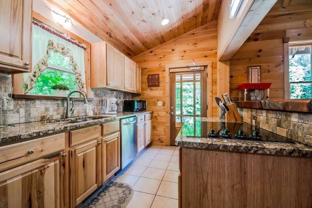 A wooden cabin interior with a kitchen featuring granite countertops, wooden cabinets, and a stone backsplash.