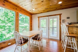 Um quarto com painéis de madeira, uma mesa de jantar e cadeiras, janelas amplas e uma porta que dá para o exterior.