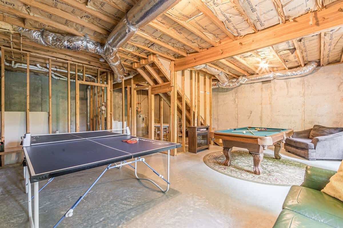 A room with a ping pong table, pool table, and leather sofa.