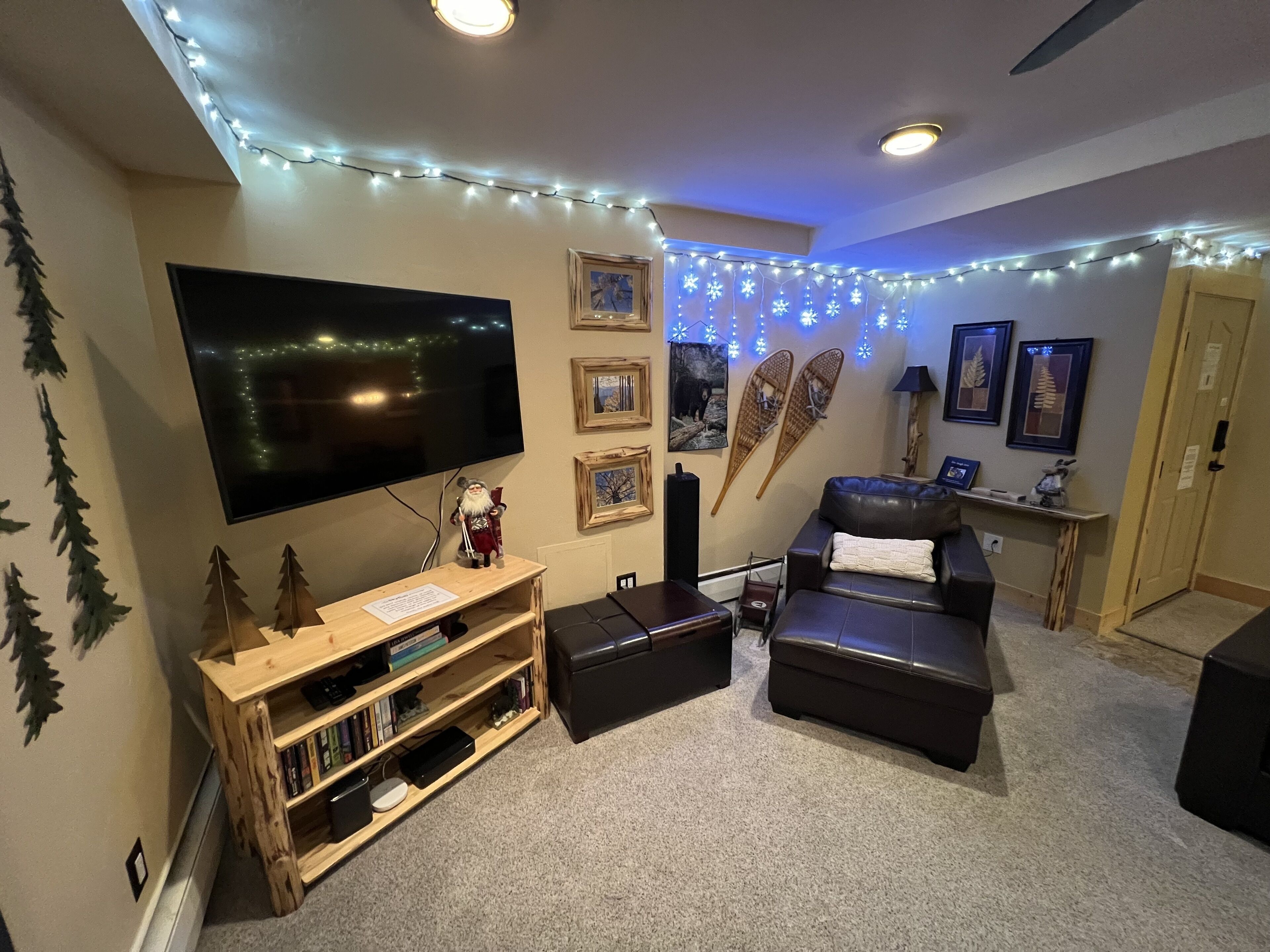 Een gezellige woonkamer met een flatscreen televisie, een houten tv-meubel, een leren bank en decoratieve verlichting.
