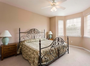 A bedroom with a four-poster bed, two bedside tables with lamps, a ceiling fan, and large windows with blinds. - Kinsale (Davenport)