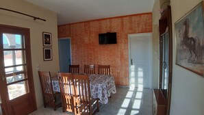 Ein Essbereich mit einem Tisch für vier Personen, einem an der Wand befestigten Fernseher und einer Tür zu einem anderen Raum.