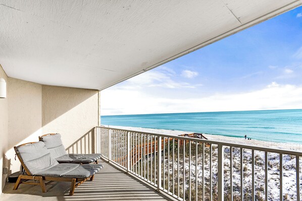 A balcony with two lounge chairs and a view of the beach.