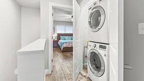 A laundry room with two washing machines, a white cabinet, and a bedroom visible through an open door. - Gulf Front 2BR Condo• 2 Balconies • Panoramic Gulf Views • Starboard Village 422 (Pensacola Beach)