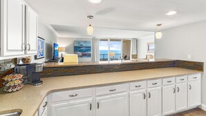 A modern kitchen with white cabinets, a stone backsplash, and a large island with a coffee maker and bowls. - Gulf Front 2BR Condo• 2 Balconies • Panoramic Gulf Views • Starboard Village 422 (Pensacola Beach)
