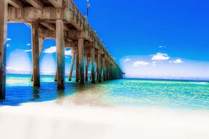 A pier extending into a clear blue sea with a sandy beach at the end.