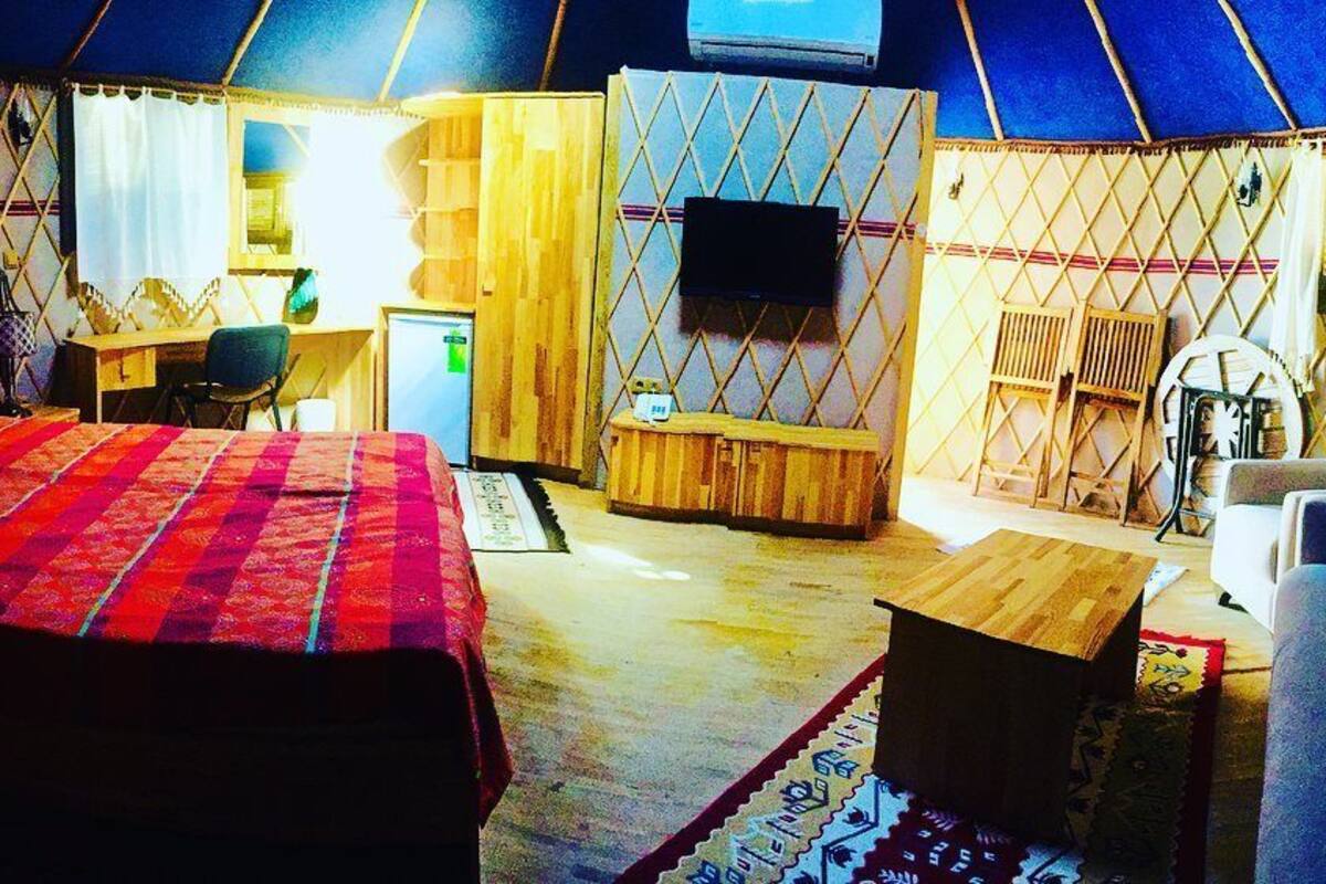 A tent-style room with a bed, desk, chair, TV, and seating area.