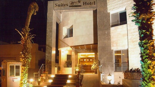 Ein Hotel Eingang mit einem Schild, auf dem 'Suites Belly Hotel' steht, mit modernem Design und einer Treppe, die zum Eingang führt, sowie dekorativen Pflanzen rund um den Eingangsbereich.