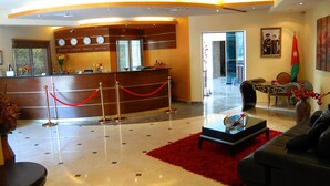 Eine Hotelhalle mit einer Rezeption, einem roten Teppich, einem schwarzen Sofa und einem gerahmten Bild an der Wand.