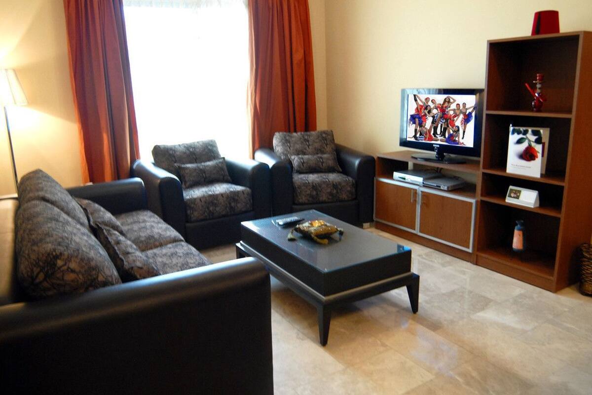 A living room with a sofa, two armchairs, a coffee table, a television, and a bookshelf.