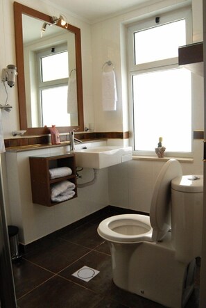 A bathroom with a toilet, sink, mirror, and window. - Beity Rose Suites Hotel (Amman)