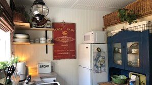 Keittiössä on valkoinen liesi, valkoinen jääkaappi ja sininen kaappi, jossa on lasiovet. Seinällä on punainen kyltti, jossa on kultaisin kirjaimin kirjoitettu teksti.
